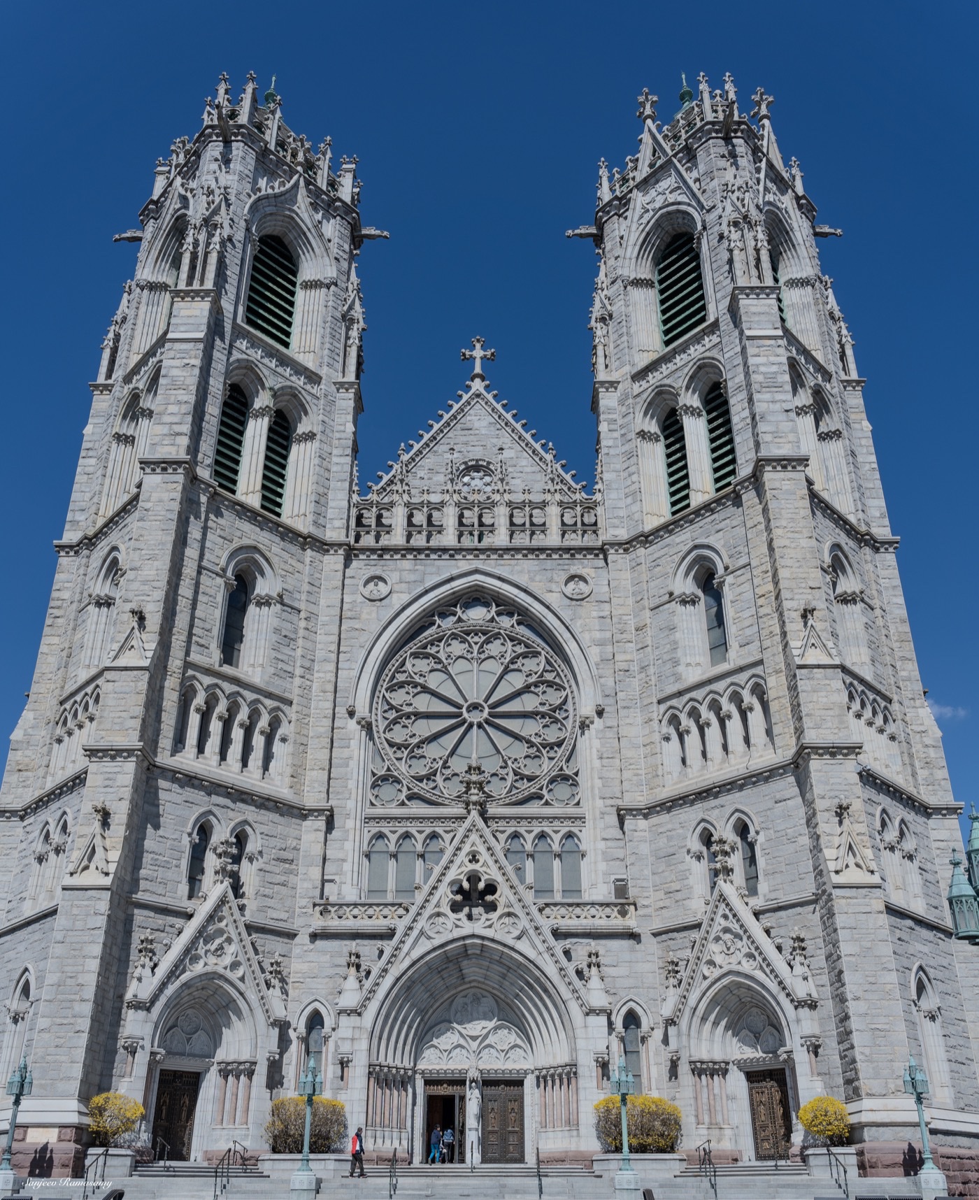 Twin-spired Gothic cathedral with a large rose window, photographed from below against a blue sky.