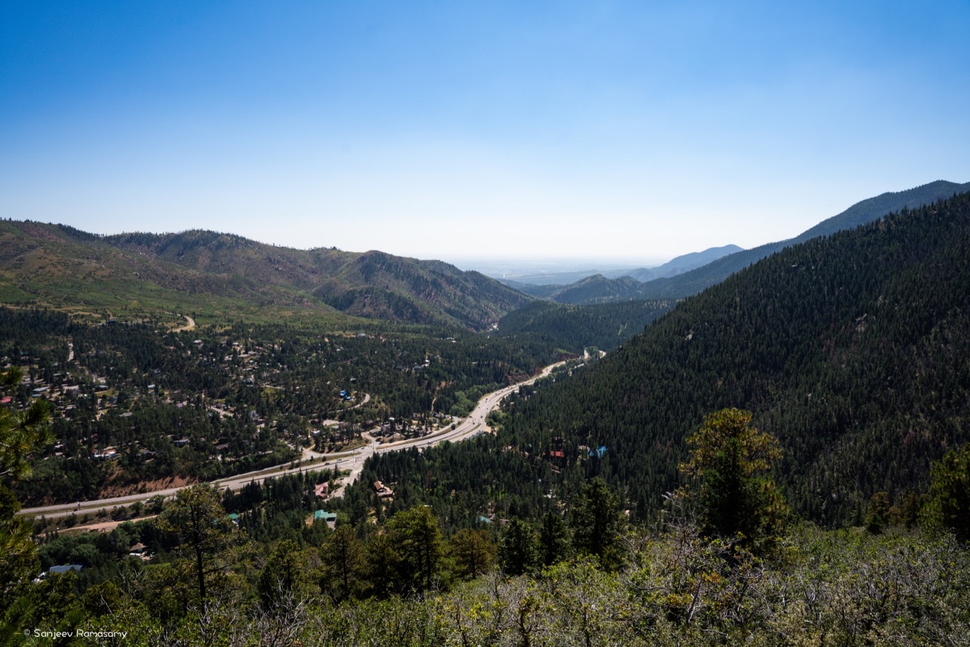 View down a forested mountain valley with a town and a winding road along its floor.