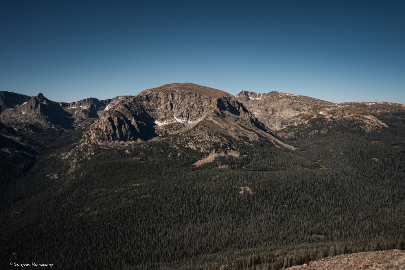 Rugged mountain peaks with patches of snow rising above a dark pine forest.