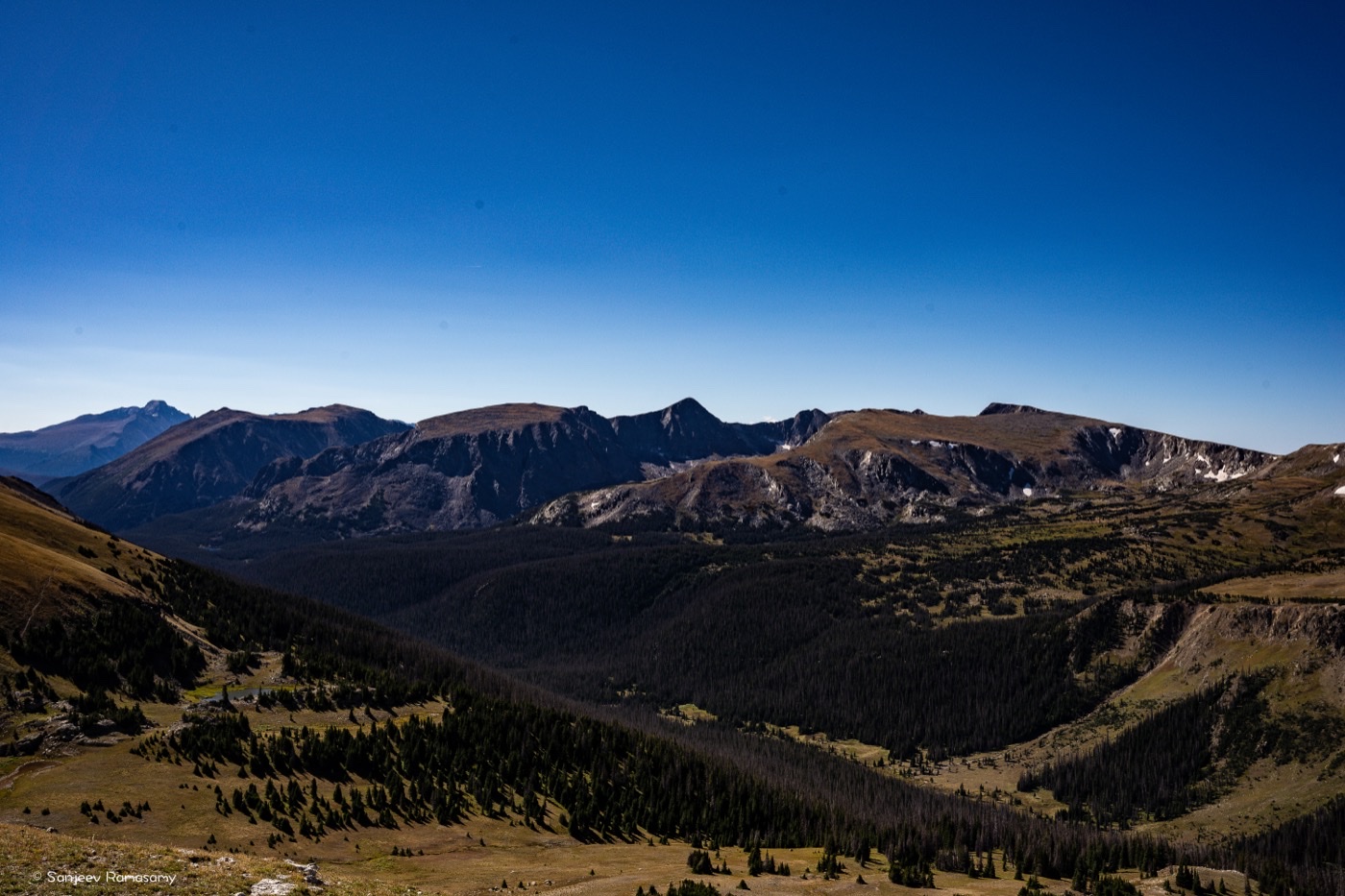 Wide view across forested valleys to a jagged mountain range under a deep blue sky.