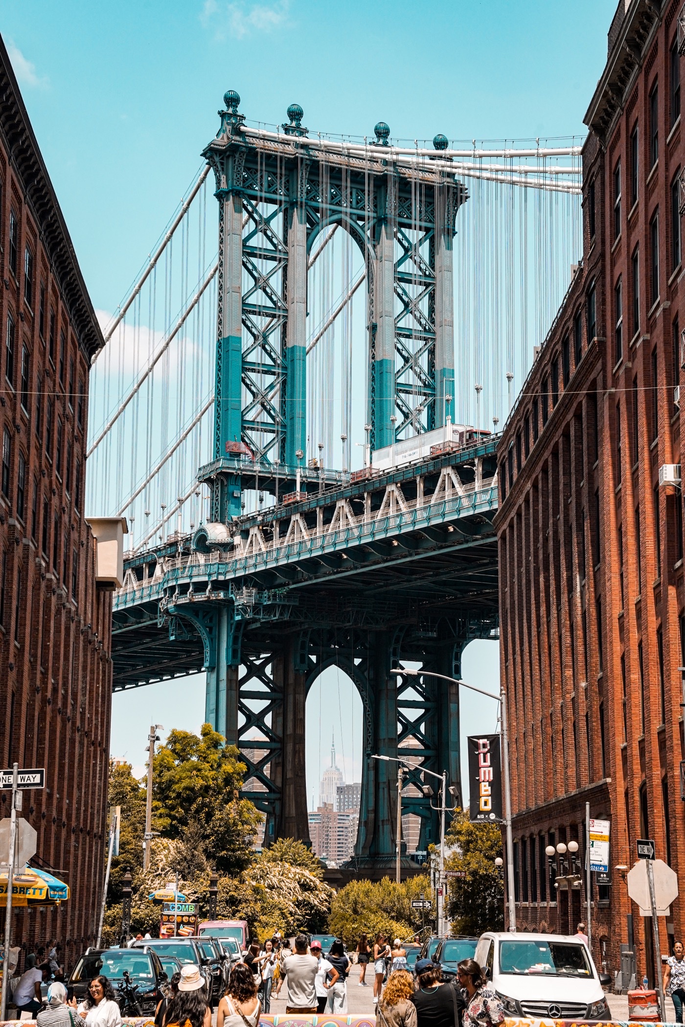 Steel suspension bridge tower framed between two red-brick buildings above a busy street.