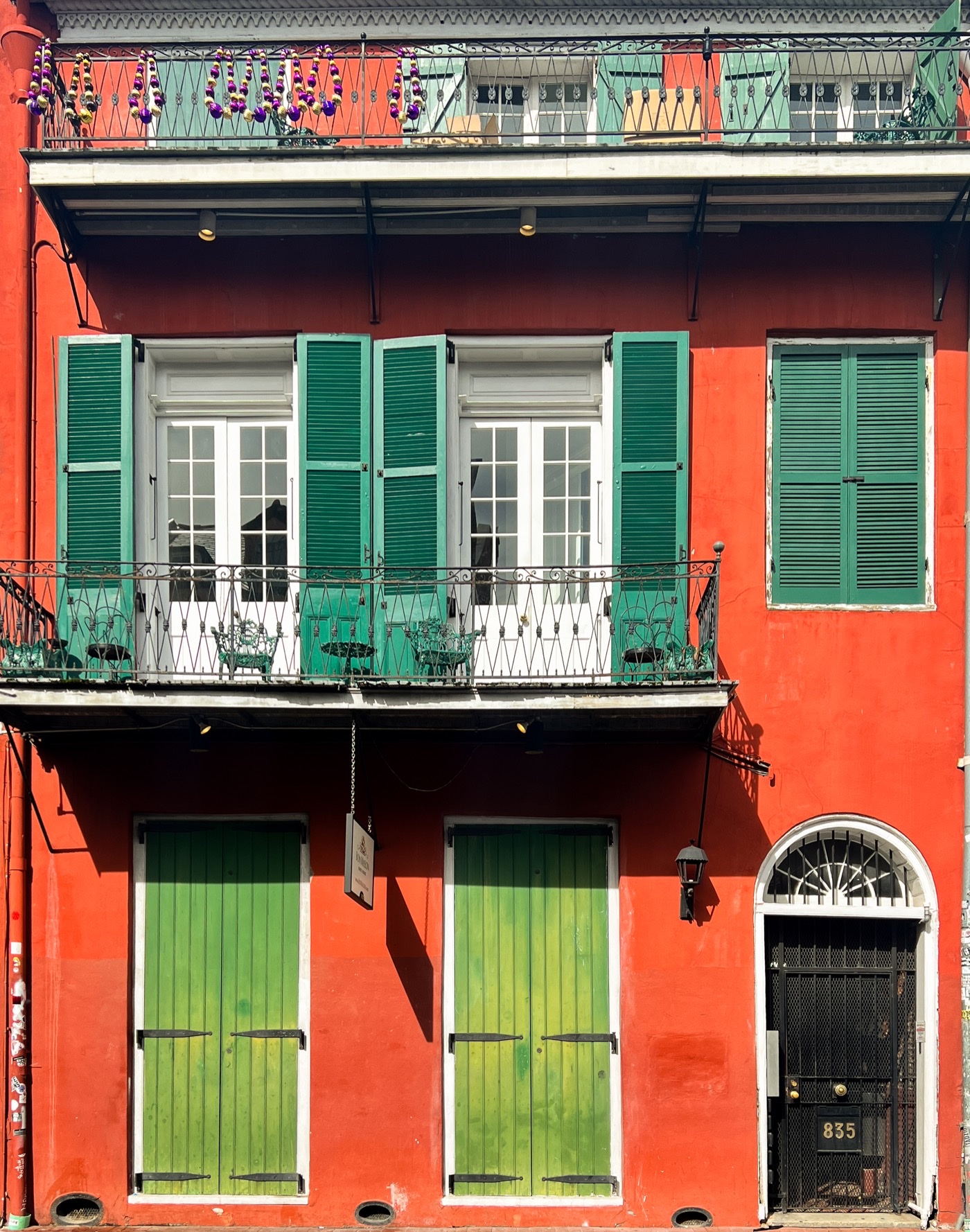 Red building with green shutters, green doors and a wrought-iron balcony, photographed straight on.